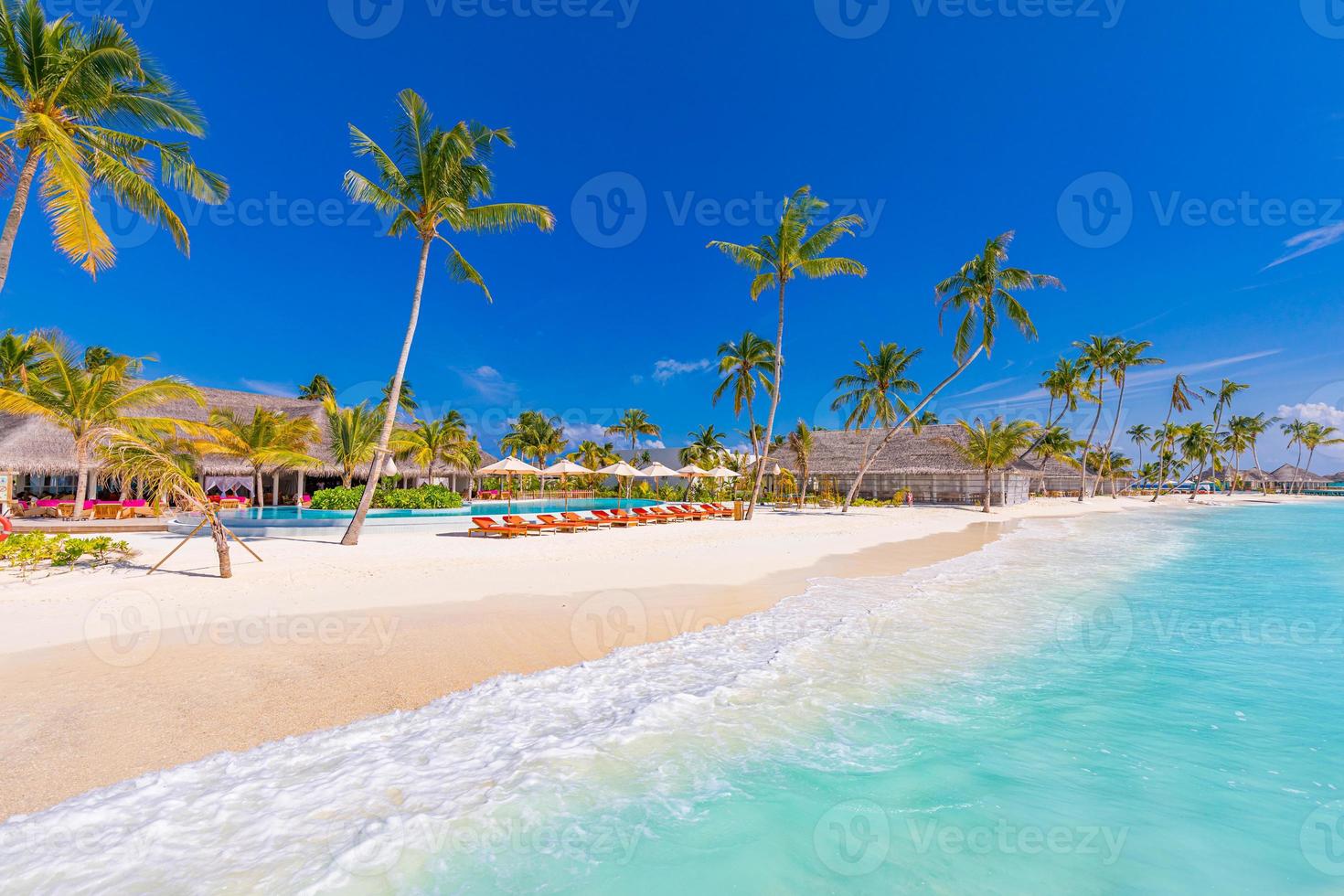 paisagem de turismo ao ar livre. luxuoso resort de praia com piscina e cadeiras de praia ou espreguiçadeiras sob guarda-sóis com palmeiras e céu azul. conceito de viagens e férias de luxo de verão foto