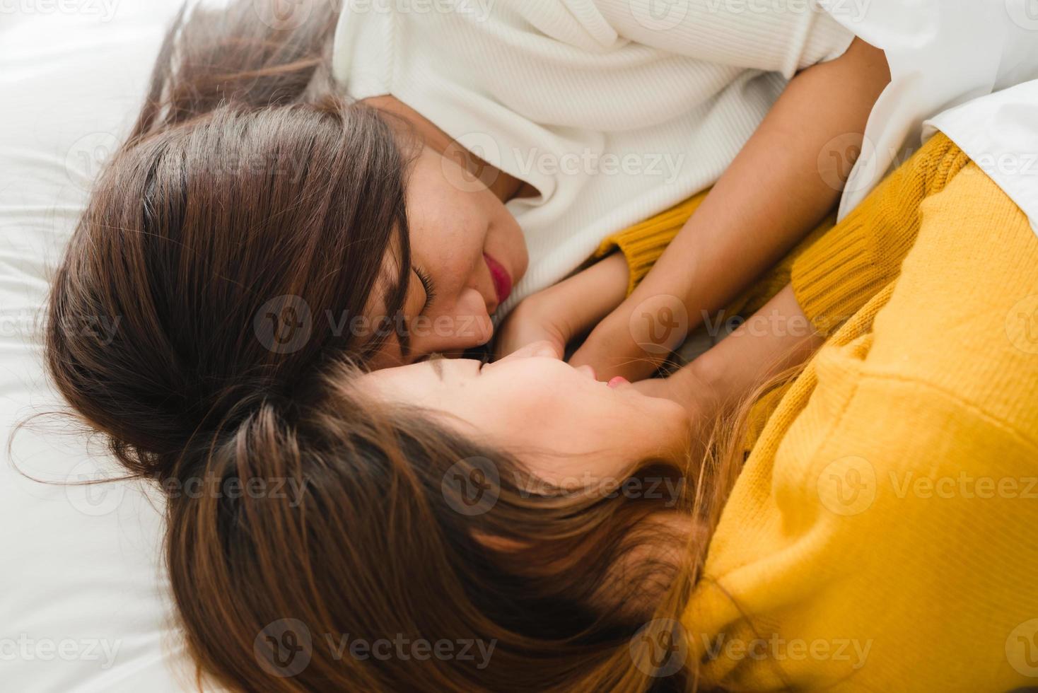 belas jovens mulheres asiáticas lgbt lésbicas casal feliz abraçando e sorrindo enquanto estavam deitados juntos na cama, debaixo do cobertor em casa. mulheres engraçadas depois de acordar. conceito de casal de lésbicas lgbt juntos dentro de casa. foto