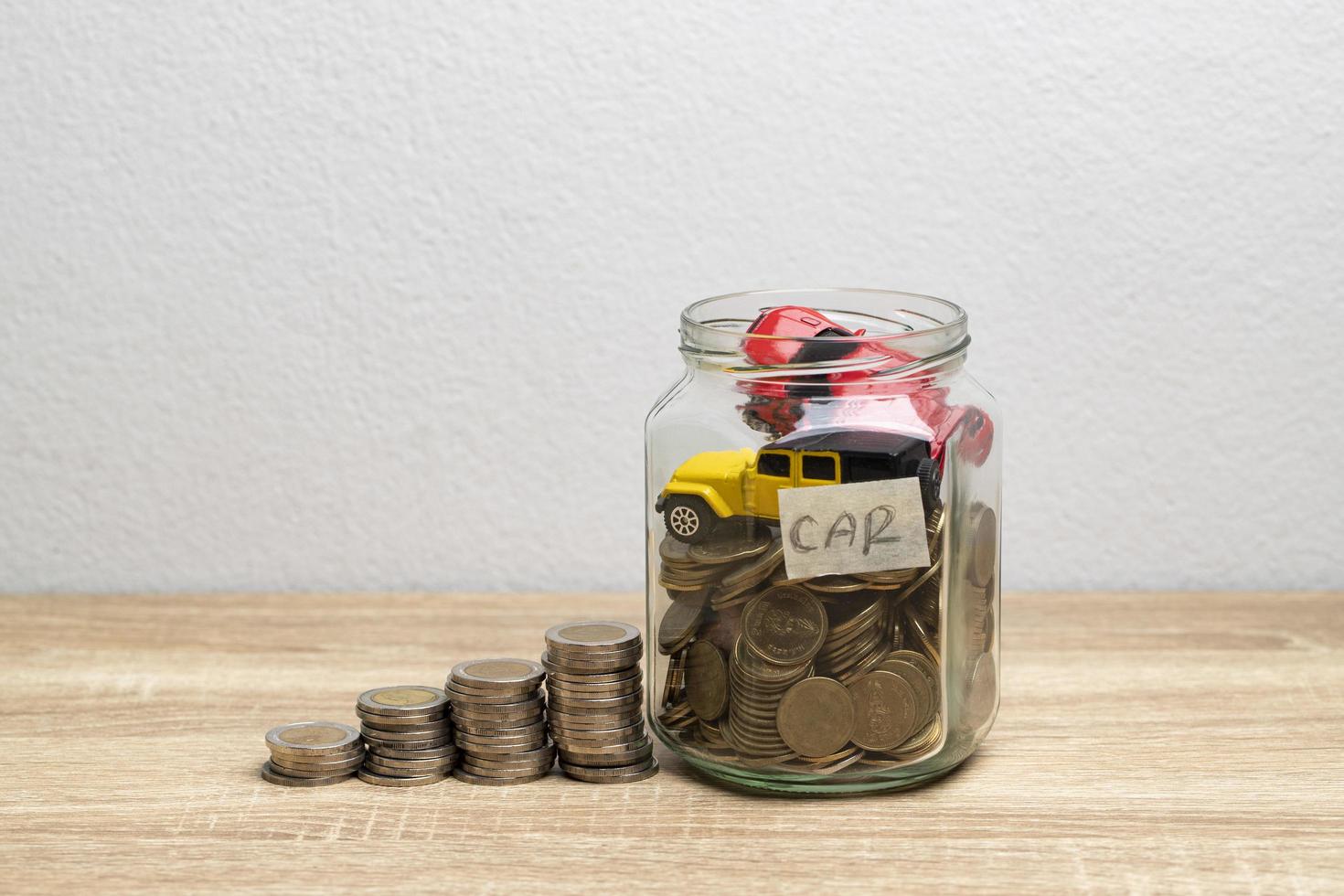 moedas e carros em uma jarra de vidro para economizar dinheiro na mesa com fundo branco foto