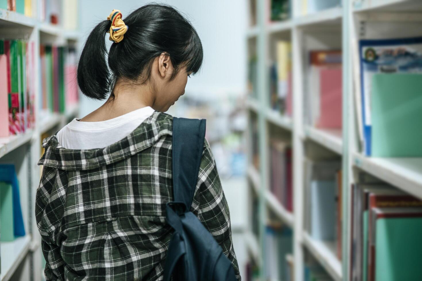 mulheres carregando uma mochila e procurando livros na biblioteca. foto