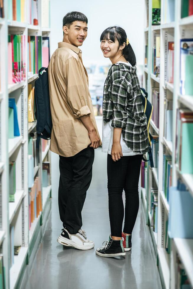 homens e mulheres carregando mochilas e procurando livros na biblioteca. foto