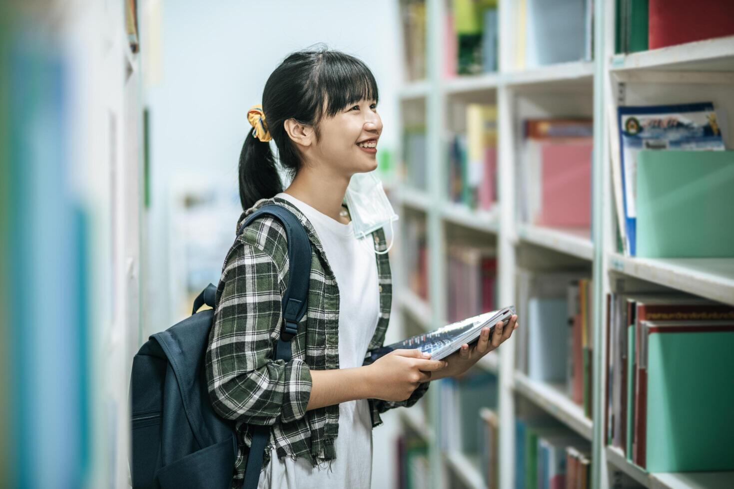 mulheres carregando uma mochila e procurando livros na biblioteca. foto