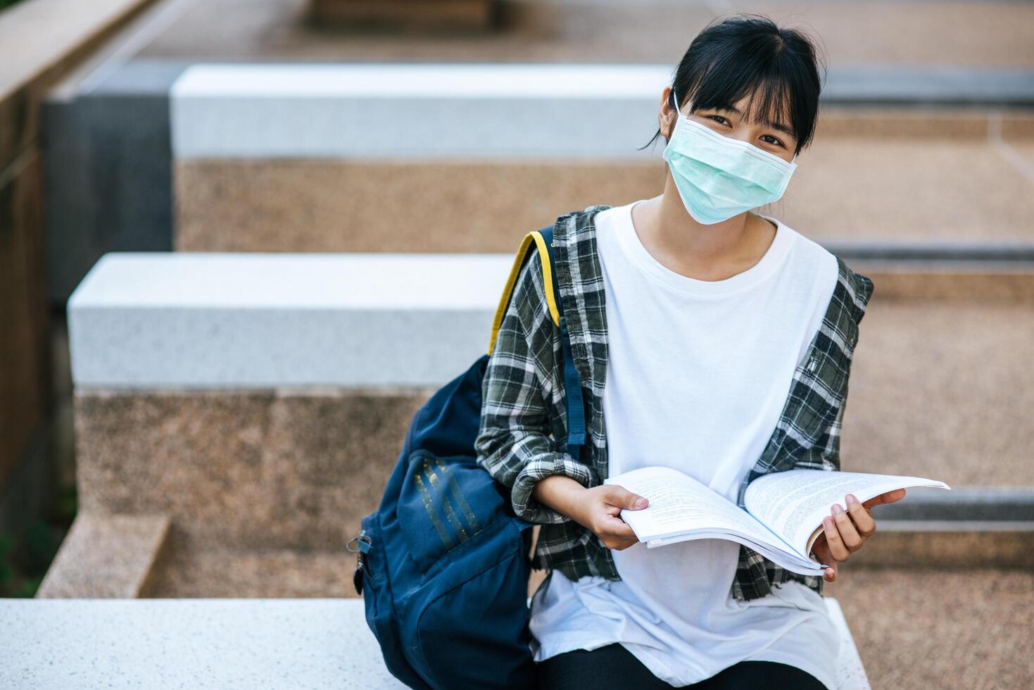 estudantes do sexo feminino usando máscaras e livros nas escadas. foto