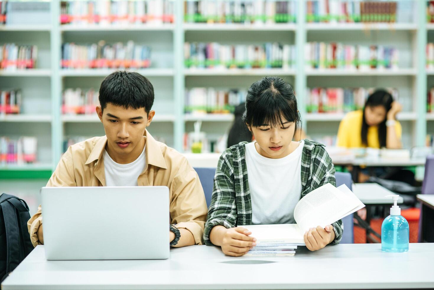 as mulheres lêem livros e os homens usam laptops para procurar livros nas bibliotecas. foto