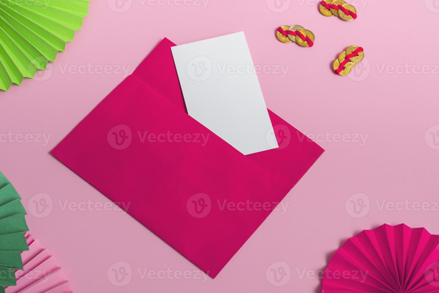 um envelope rosa com um cartão em branco sobre um fundo vermelho com um leque de papel e dinheiro chinês. close up, copie o espaço foto