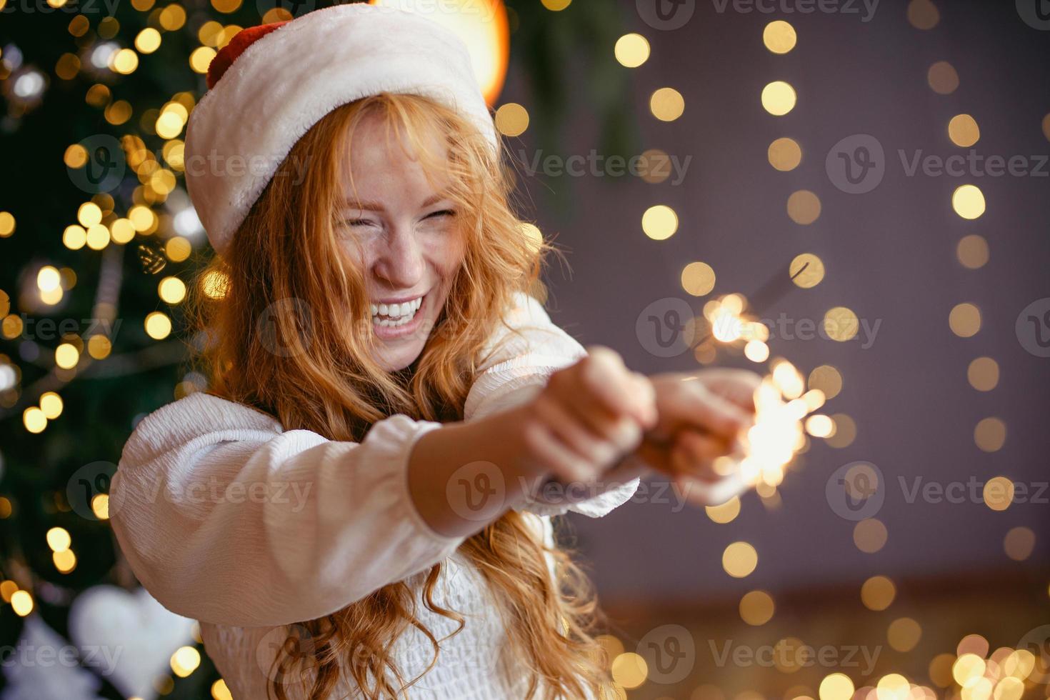 adorável garota ruiva com um chapéu de Papai Noel com estrelinhas nas mãos sorrindo para a câmera foto