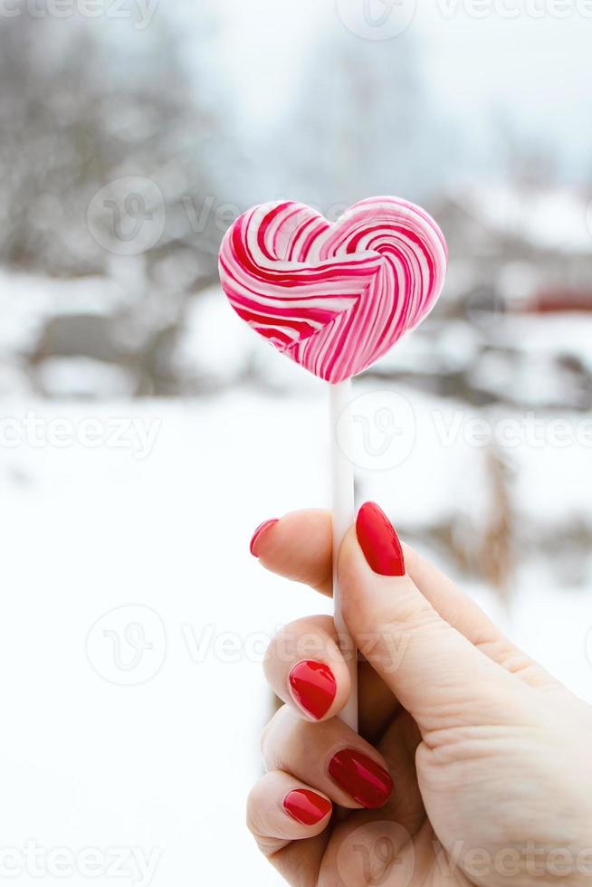 mão segura pirulito rosa. doce coração, símbolo do dia dos namorados. foto