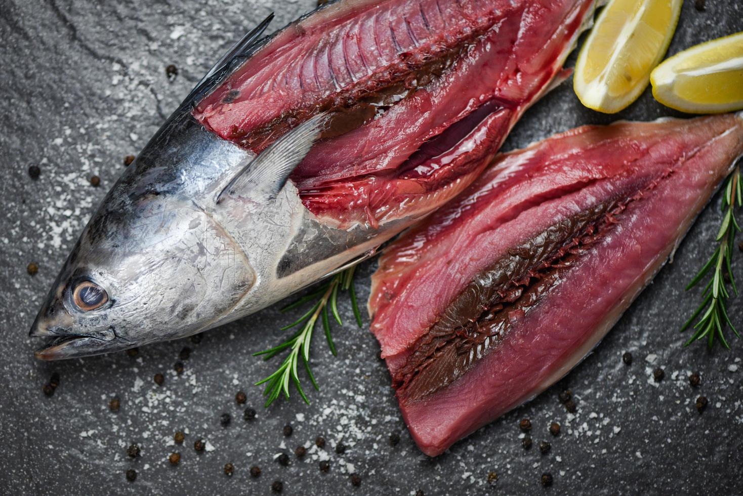 filé de peixe fresco fatiado para bife ou salada com ervas, especiarias, alecrim e limão, peixe cru, frutos do mar no fundo da placa preta atum longtail, ingredientes de filé de atum oriental para cozinhar alimentos foto