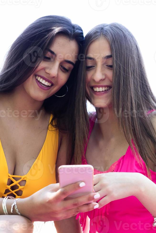 duas adolescentes de maiô sentadas no gramado da piscina assistindo ao celular foto