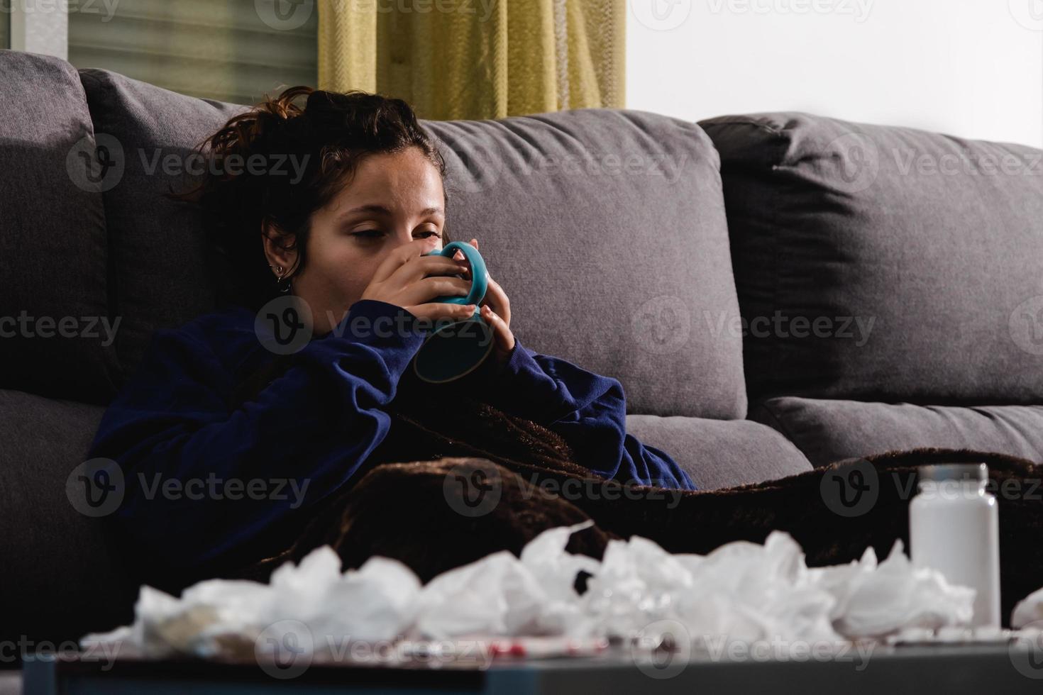 mulher doente no sofá em casa tomando uma bebida quente foto