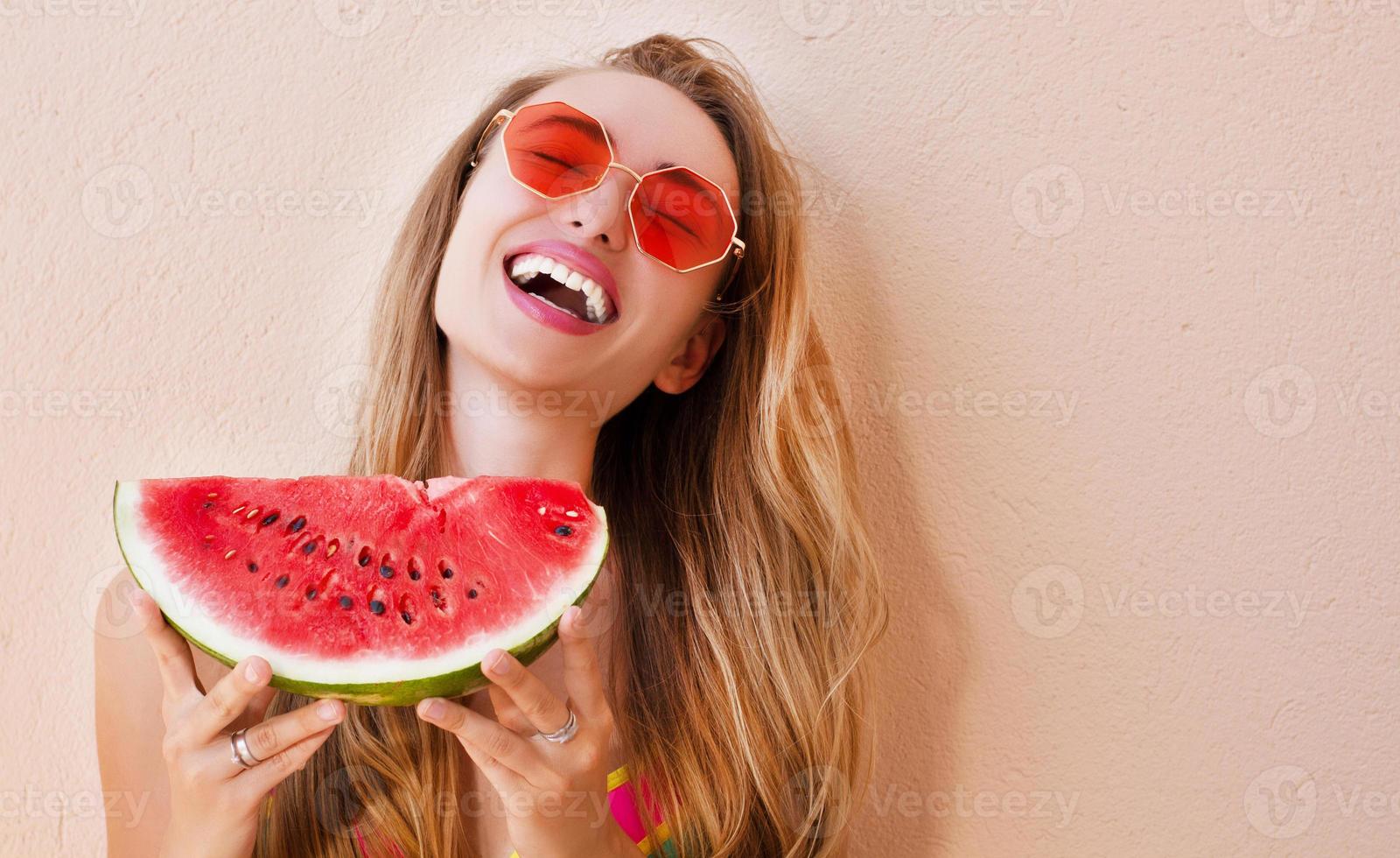 garota sexy em óculos de sol vermelhos tem uma melancia cortada nas mãos. mulher feliz em óculos de sol vermelhos da moda cópia espaço foto