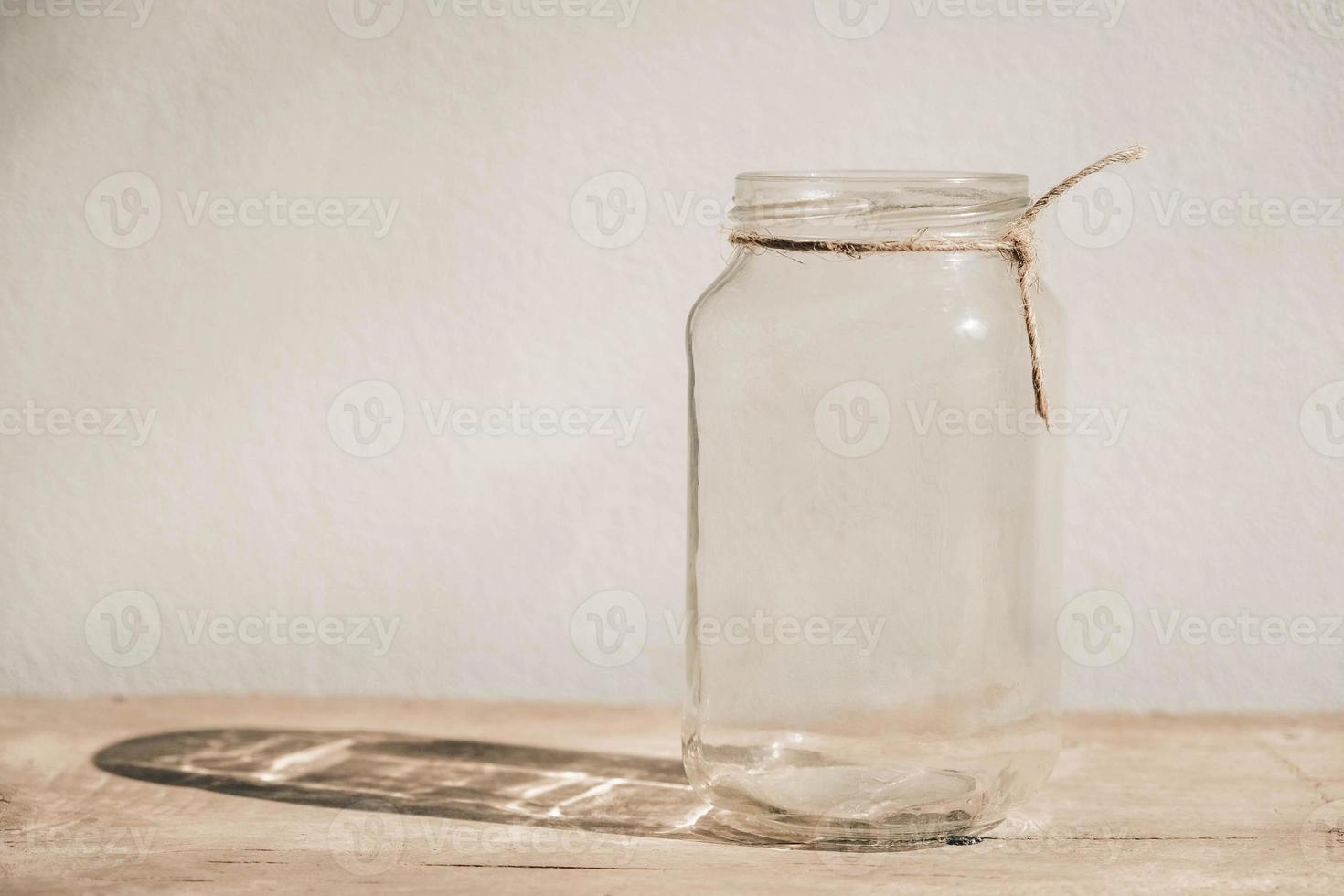 frasco de vidro transparente na mesa de madeira no fundo da parede branca foto