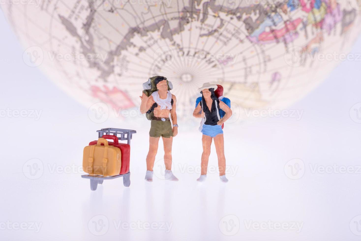 Feche de mochileiros em miniatura e turistas com a terra no fundo para o conceito de viagens foto