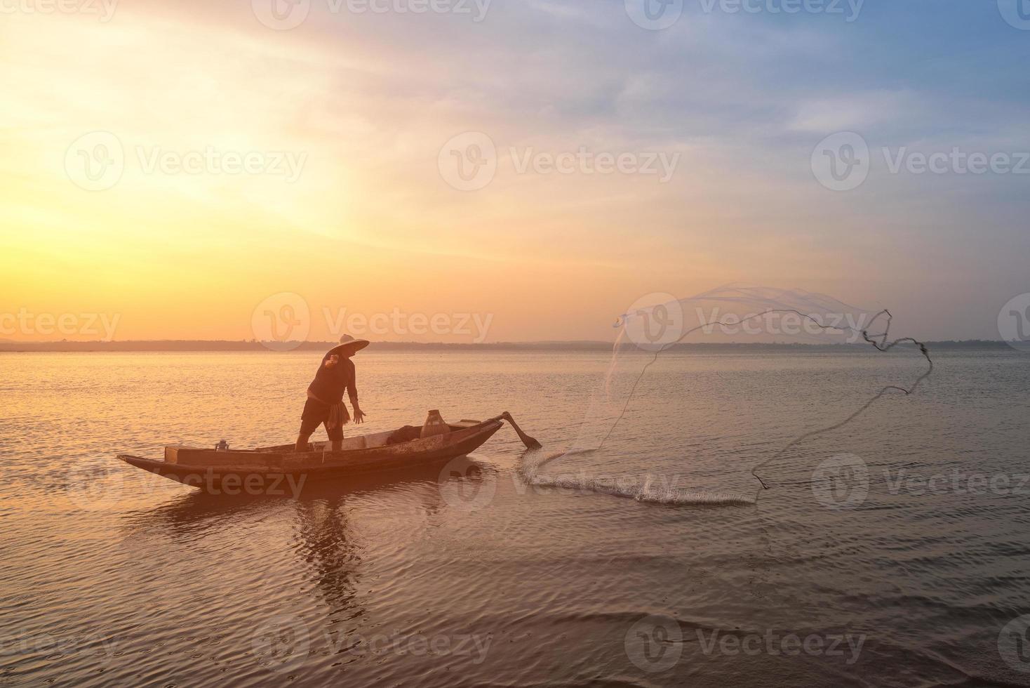 pescador asiático em um barco de madeira jogando uma rede para pegar peixes de água doce no rio da natureza no início durante o nascer do sol foto