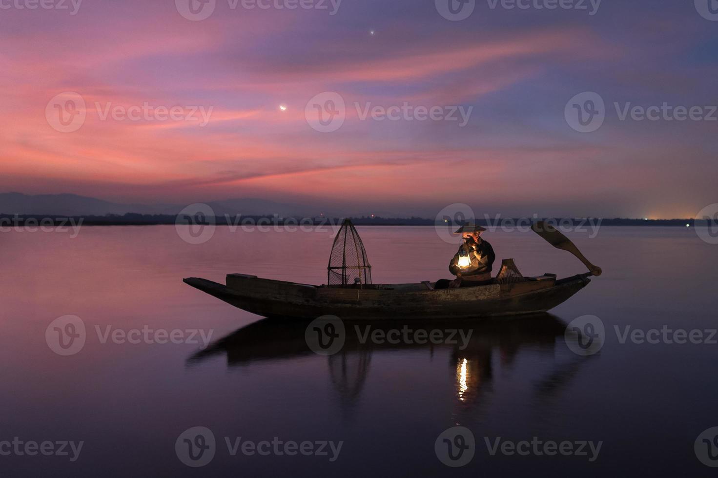 pescador asiático em um barco de madeira procurando peixes de água doce no rio da natureza no início da manhã antes do nascer do sol foto