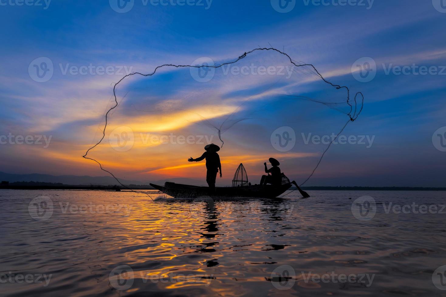 pescador asiático em um barco de madeira jogando uma rede para pegar peixes de água doce no rio da natureza no início durante o nascer do sol foto