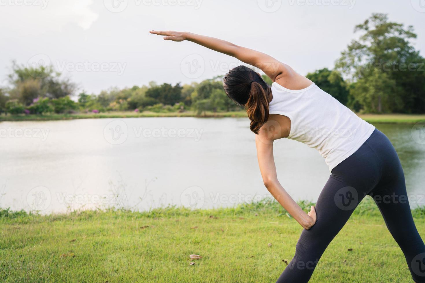 mulher jovem e saudável corredor asiático aquece o corpo, alongamento antes do exercício e da ioga perto do lago no parque, sob a luz quente da manhã. fitness de estilo de vida e mulheres ativas exercem no conceito de cidade urbana. foto