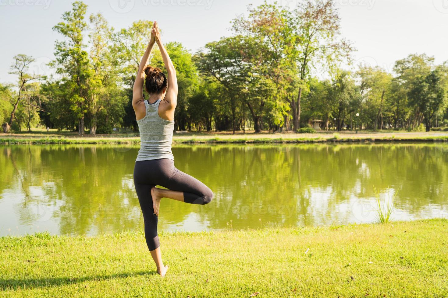 jovem mulher asiática ioga ao ar livre, mantenha a calma e medite enquanto pratica ioga para explorar a paz interior. ioga tem bons benefícios para a saúde perto do lago no parque. esporte e conceito de estilo de vida saudável. foto