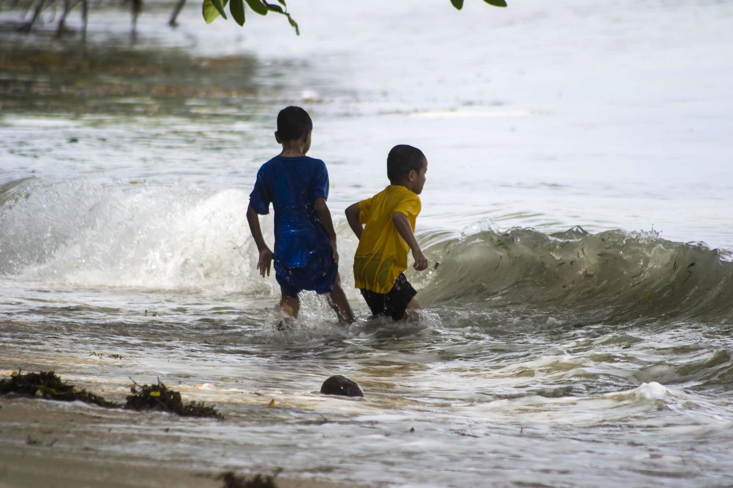 sorong, oeste de papua, indonésia, 12 de dezembro de 2021. meninos brincando contra as ondas na praia foto