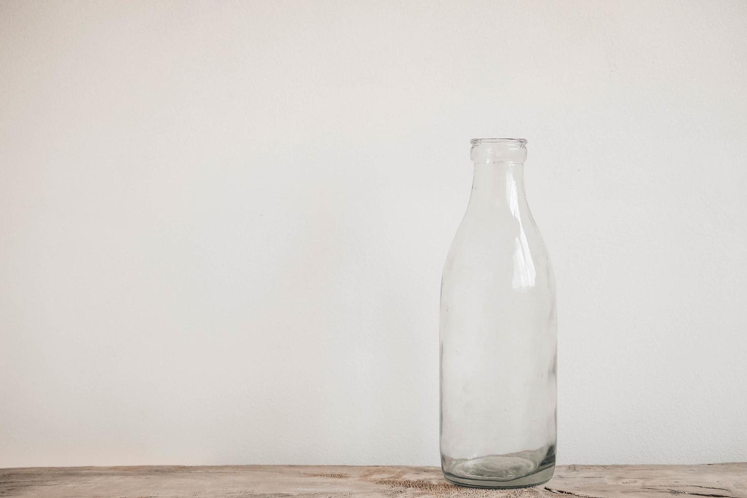 garrafa de vidro transparente na mesa de madeira no fundo da parede branca foto