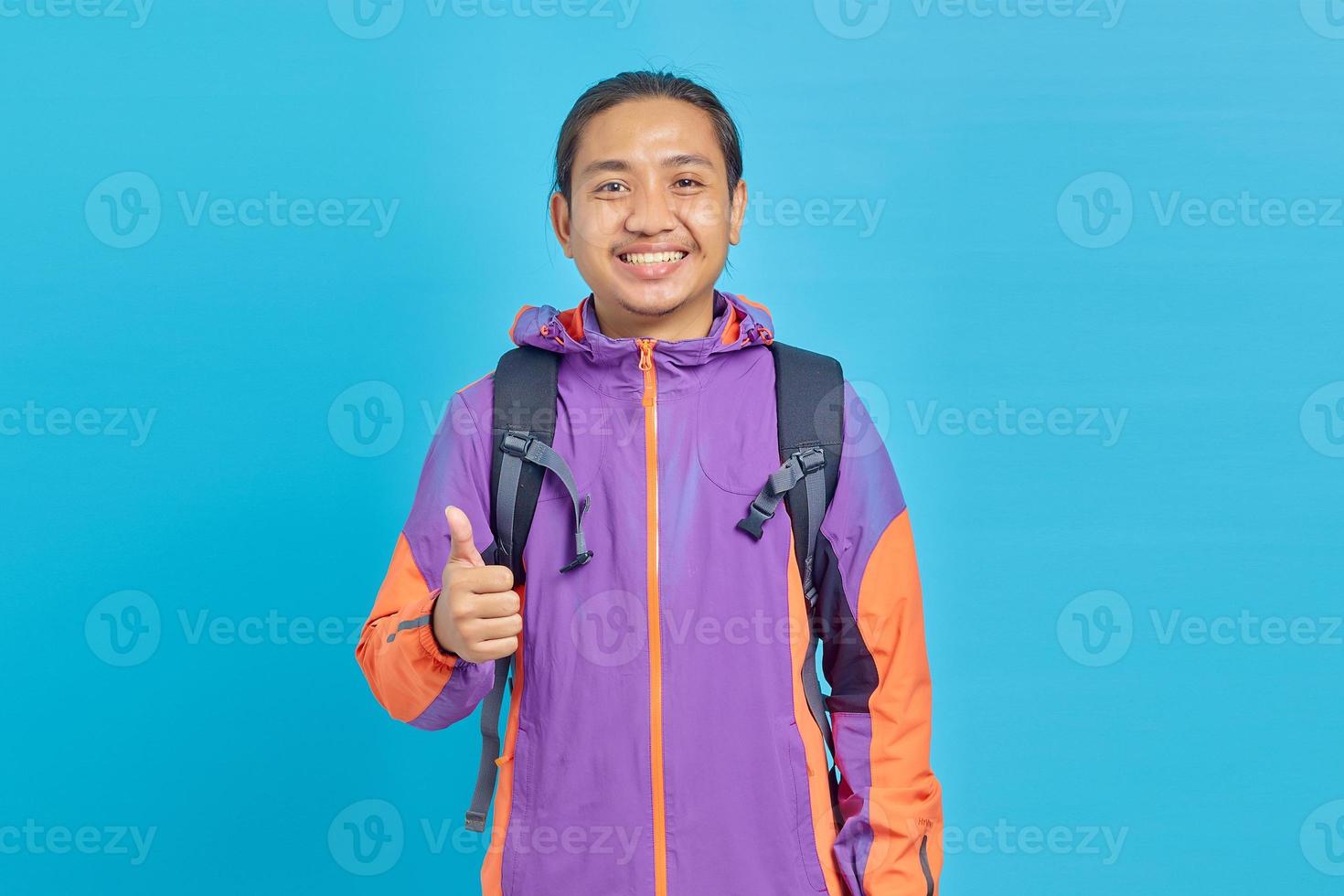 jovem asiático sorridente mostrando aprovação com gesto de polegar para cima no fundo azul foto