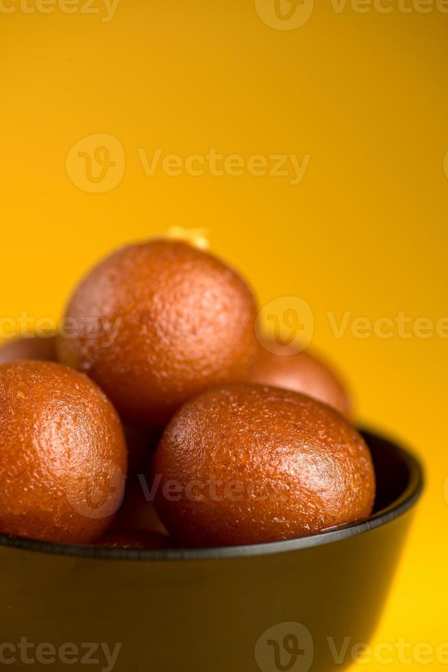 sobremesa indiana ou prato doce gulab jamun em uma tigela sobre fundo amarelo. foto