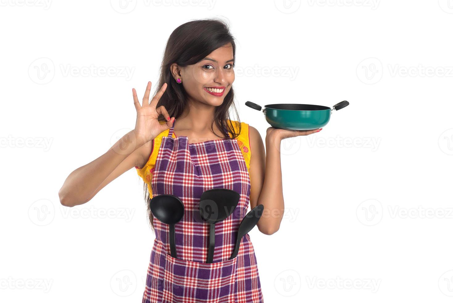 jovem mulher indiana segurando uma colher de utensílio de cozinha, estápula, concha e panela, etc. em um fundo branco foto