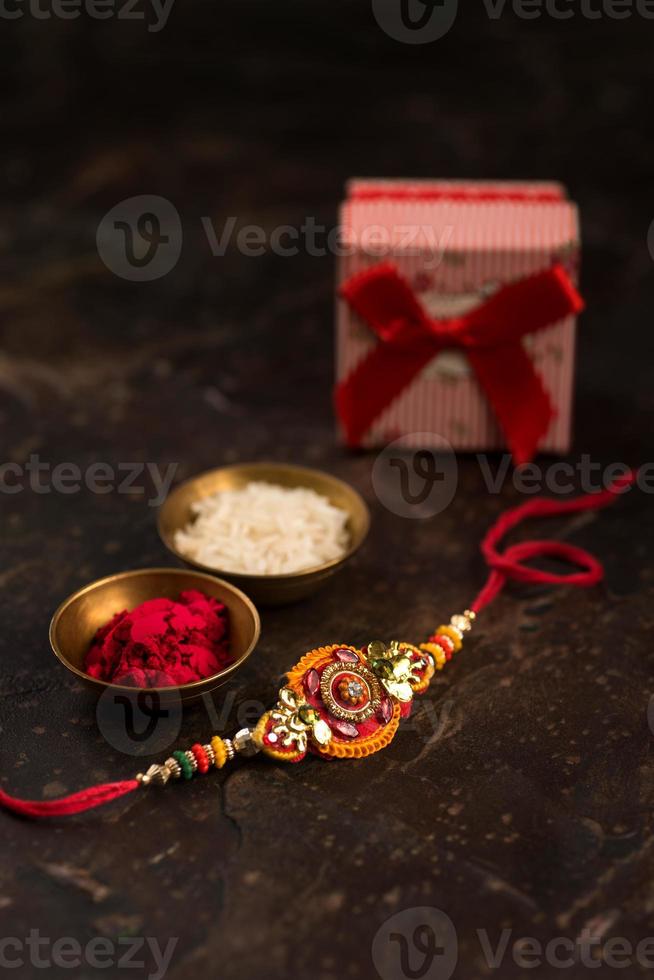 fundo raksha bandhan com um elegante rakhi, grãos de arroz, kumkum e caixa de presente. uma pulseira tradicional indiana que é um símbolo de amor entre irmãos e irmãs. foto