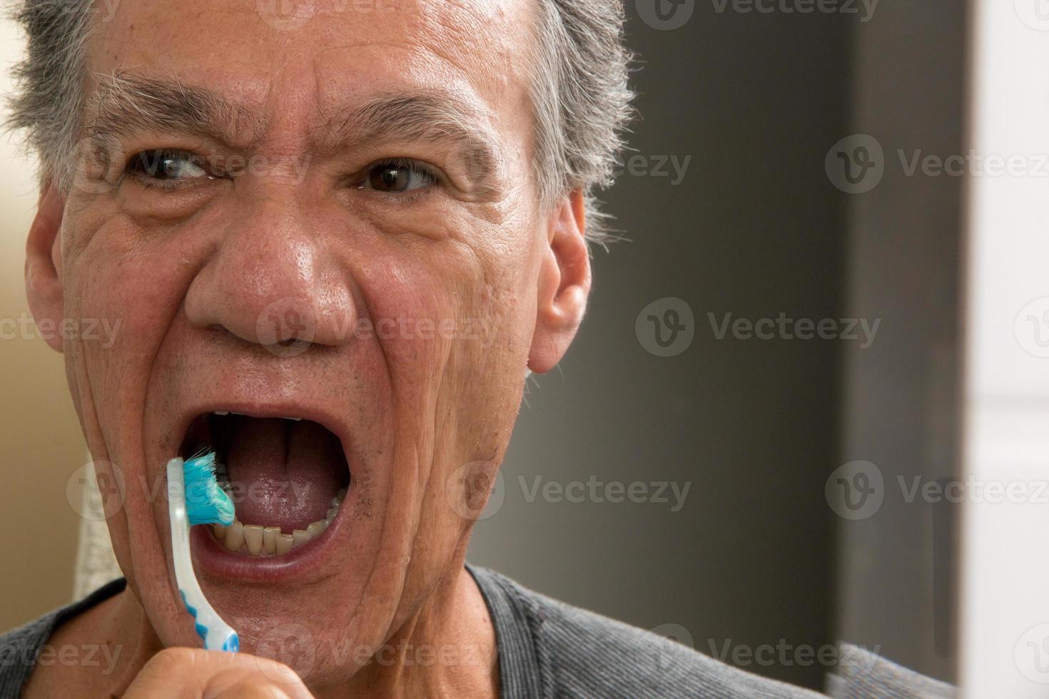 homem maduro escovando os dentes com uma escova de dentes gasta foto
