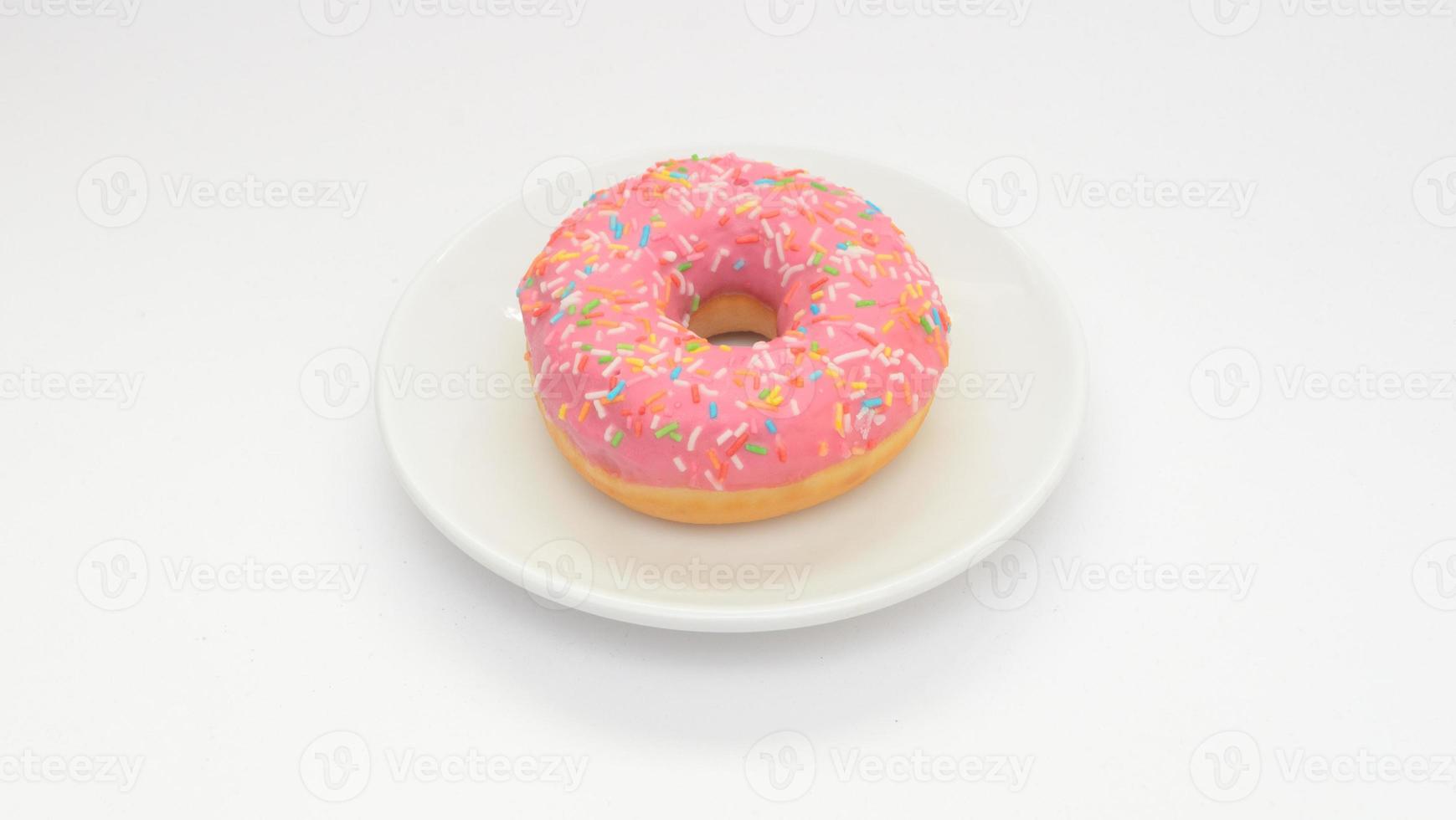 um donut com cobertura rosa no prato fundo branco. Sobremesa doce para o lanche foto