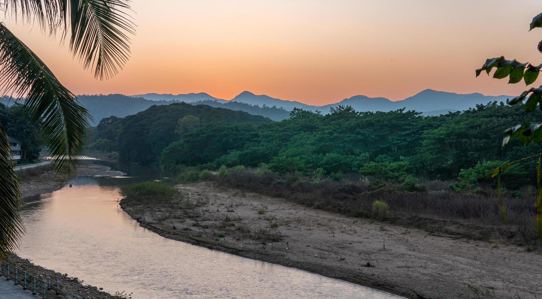 pôr do sol sobre as montanhas com rio e palmeira foto