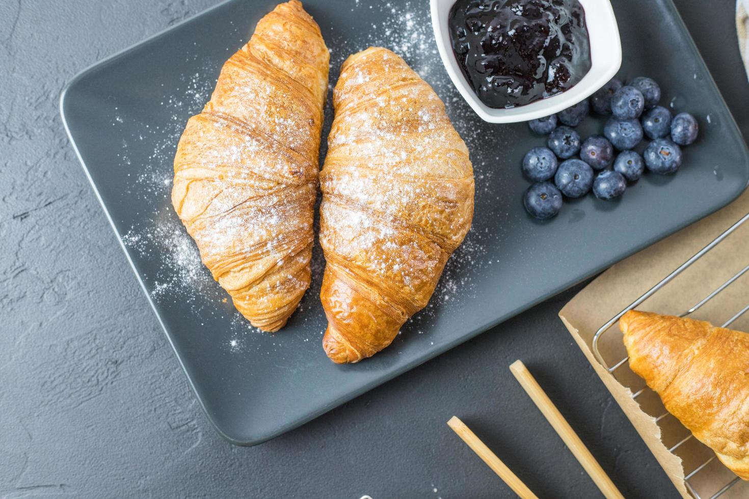 deliciosos croissants de mirtilo em um prato escuro. pequeno-almoço francês. foto