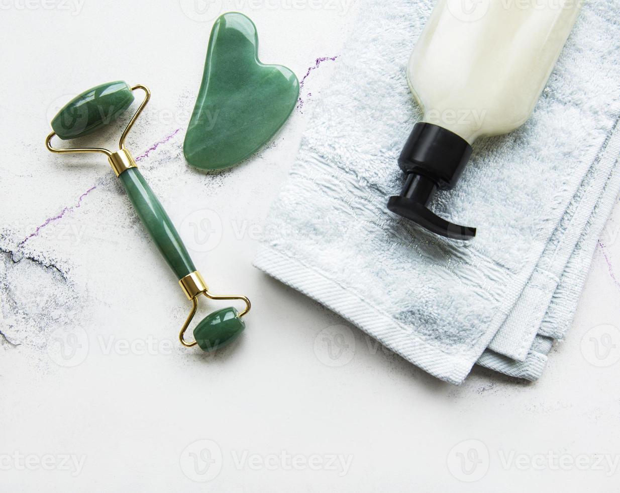 massagem facial rolo jade com produto cosmético em fundo de mármore foto