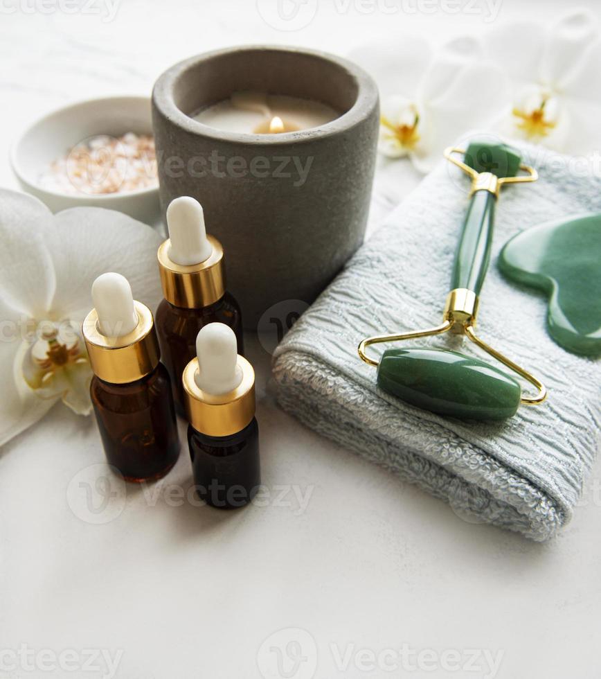 massagem facial rolo jade com produto cosmético em fundo de mármore foto