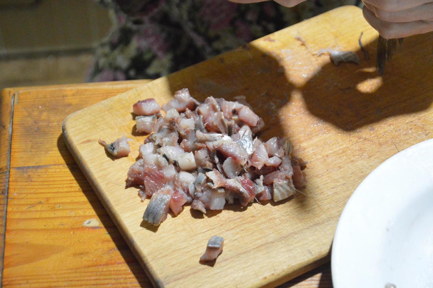 cortando arenque com uma faca na mesa da cozinha foto