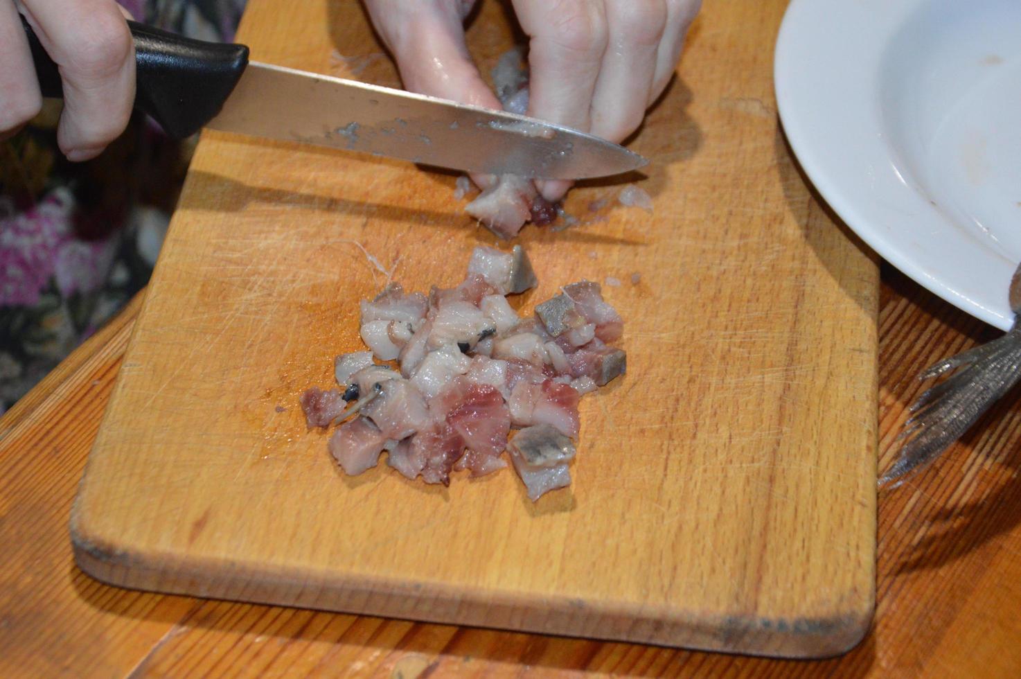 cortando arenque com uma faca na mesa da cozinha foto