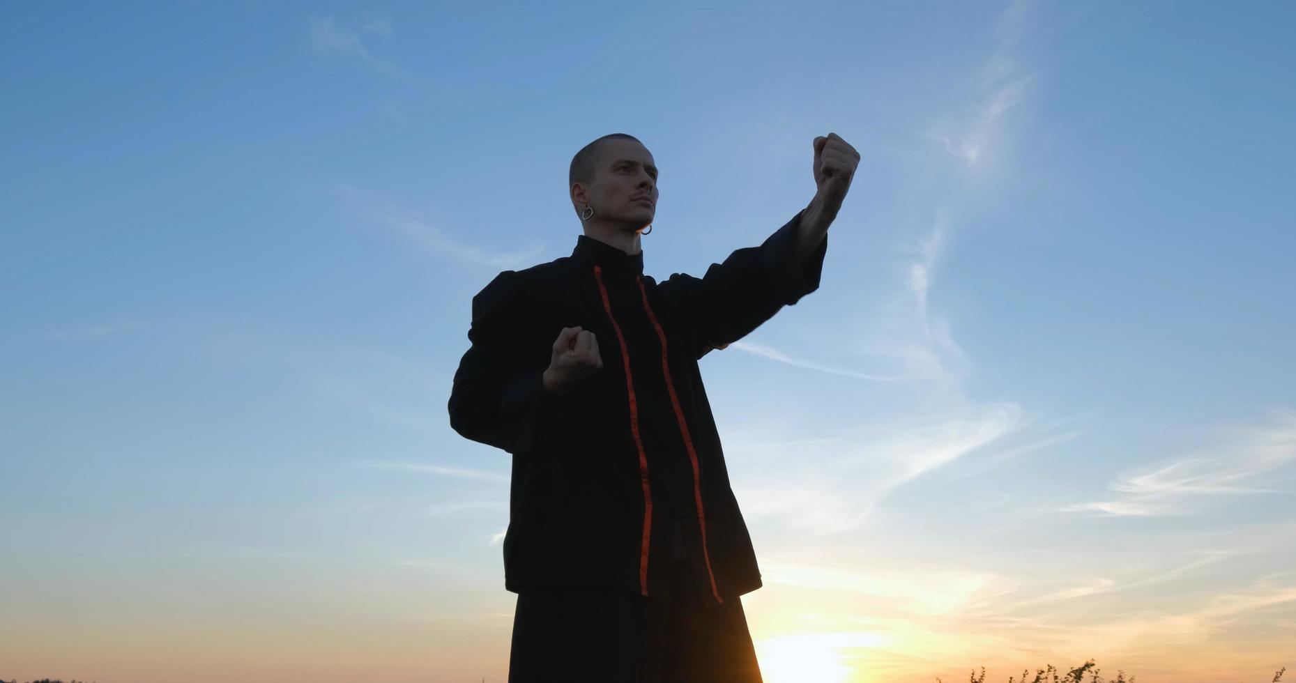 silhueta de um jovem lutador de kung fu praticando sozinho nos campos durante o pôr do sol foto