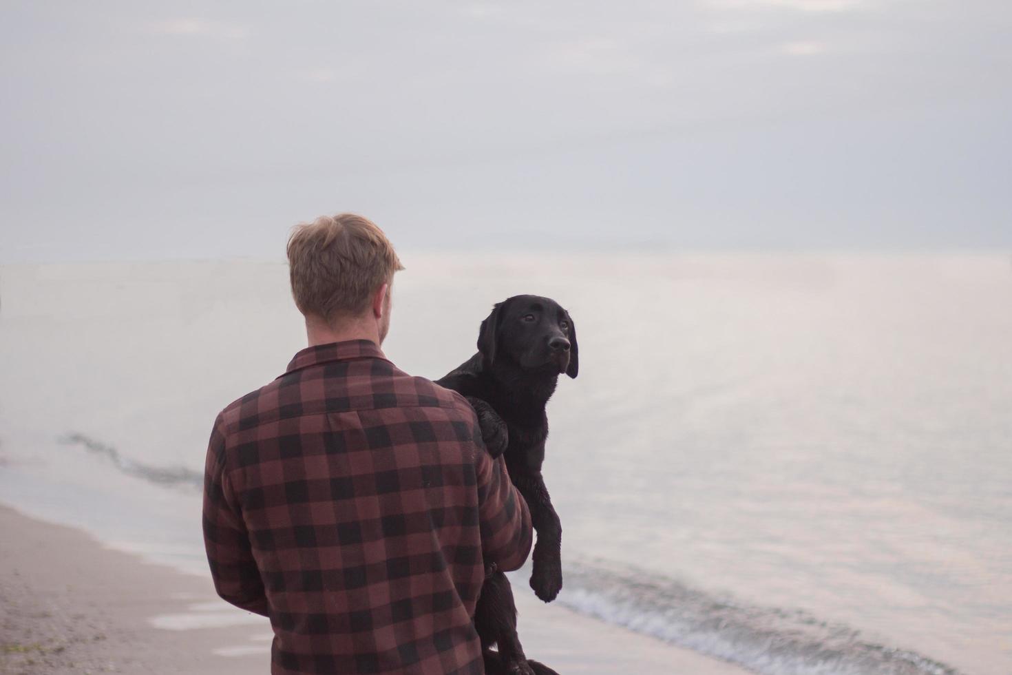 jovem caminhando na praia de manhã com cachorro preto foto