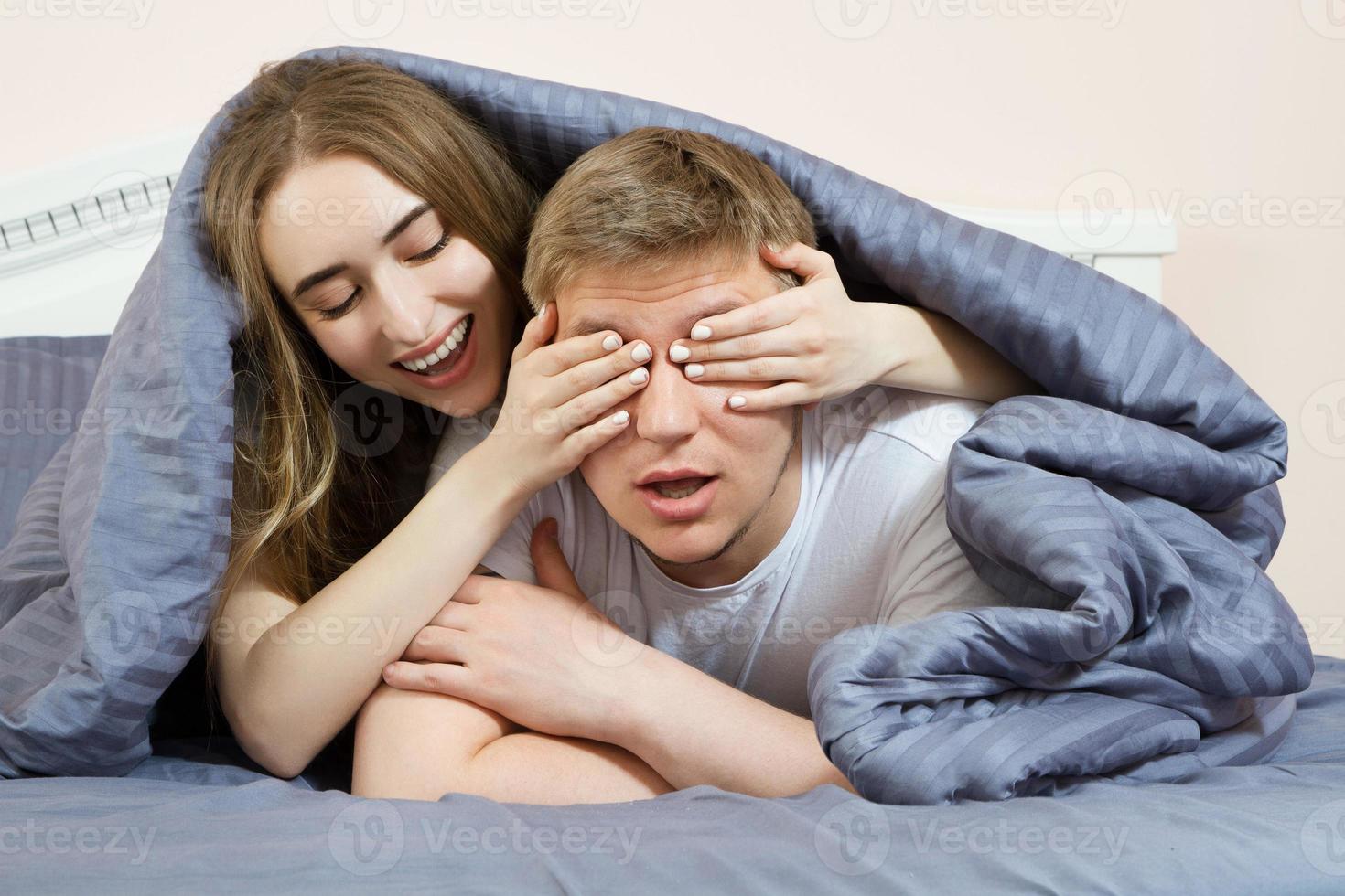 lindo casal na cama. garota fecha as mãos os olhos para o namorado na cama pela manhã foto