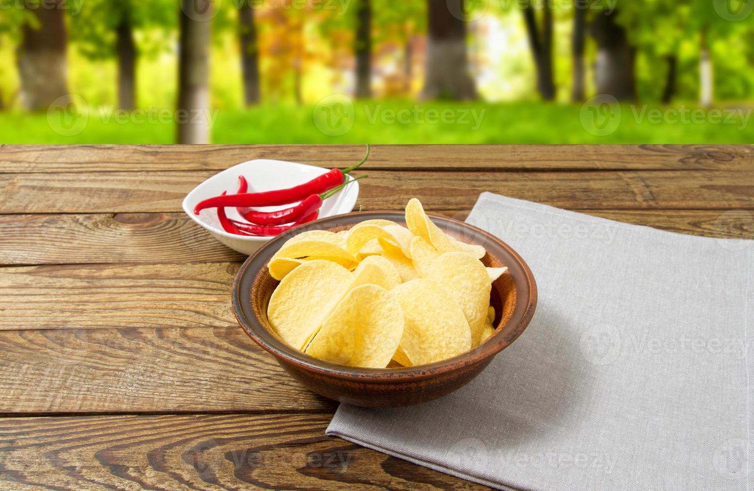 batata frita e pimenta vermelha na mesa de madeira no fundo desfocado do parque, toalha de mesa cinza foto