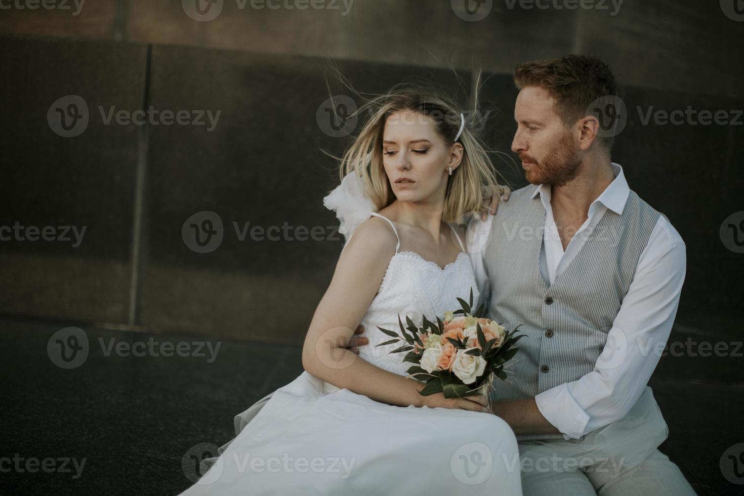 jovem casal recém-casado sentado em uma parede de blocos foto