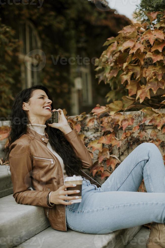 jovem mulher com telefone celular bebe café para subir as escadas ao ar livre em dia de outono foto