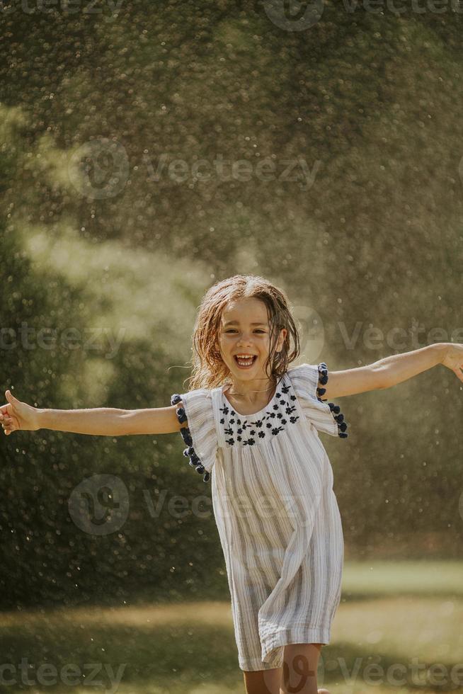 garotinha fofa se divertindo sob o aspersor de irrigação foto