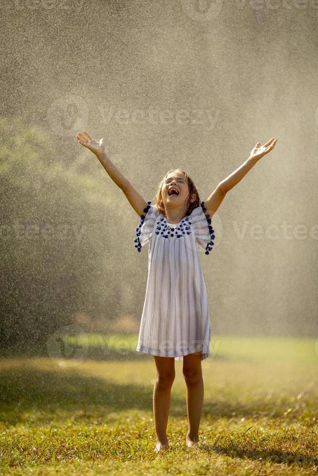 garotinha fofa se divertindo sob o aspersor de irrigação foto