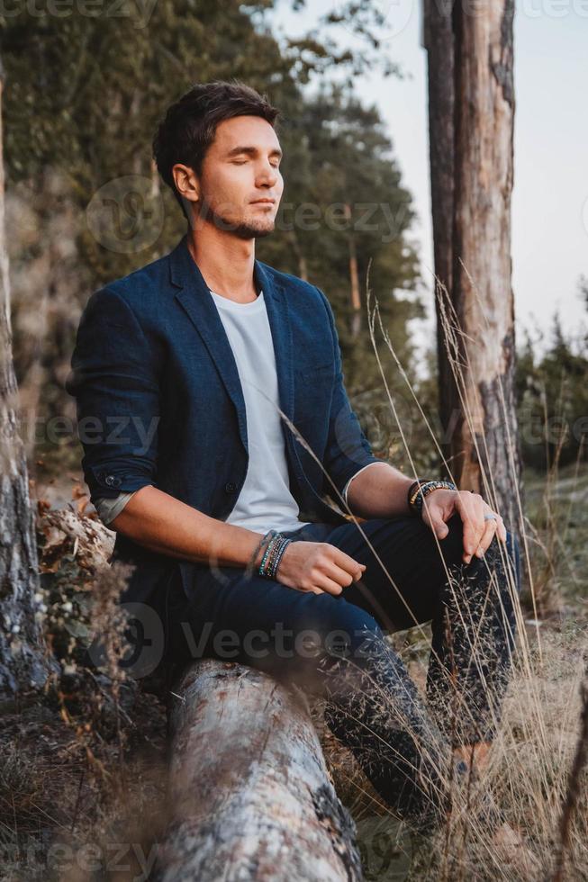 homem bonito posando ao ar livre na floresta fica em um tronco, vestindo jaqueta xadrez. lugar para texto ou publicidade foto