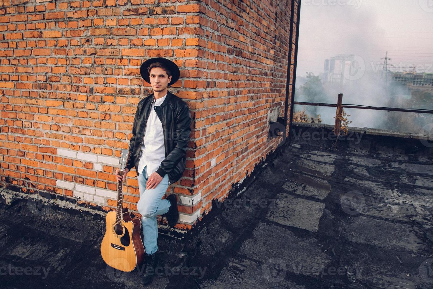 homem com uma guitarra no fundo de uma parede de tijolos foto