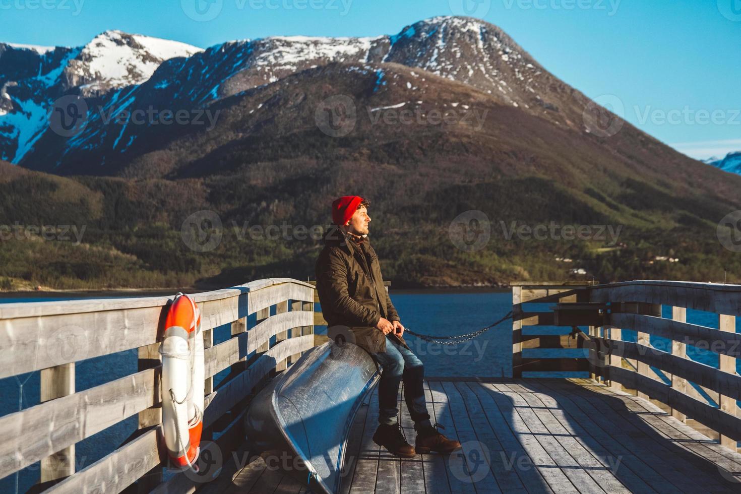 homem viajante senta-se em um píer de madeira em um fundo de lago de montanha. lugar para texto ou publicidade foto