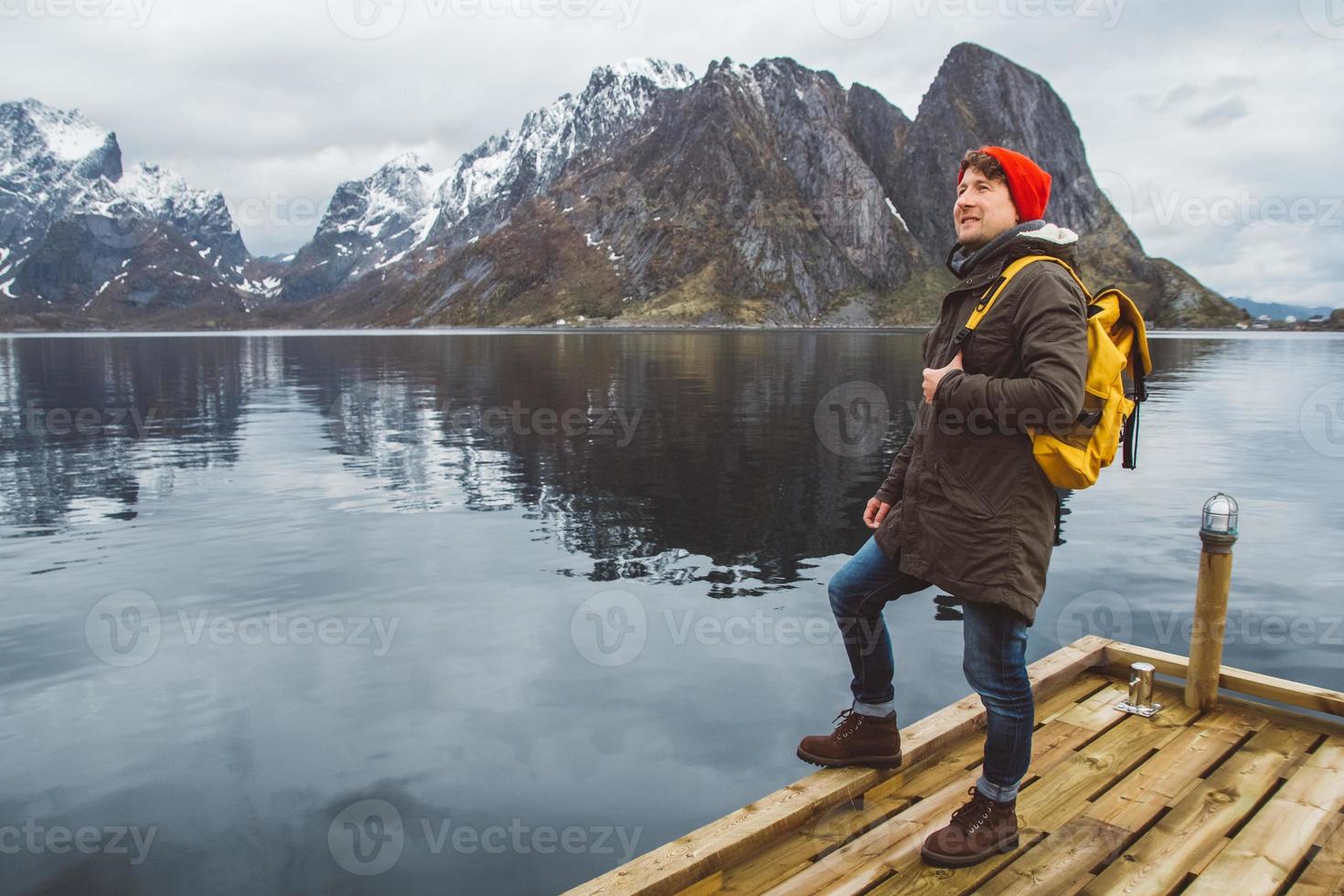 jovem com uma mochila de pé em um píer de madeira, ao fundo do lago e montanhas nevadas. lugar para texto ou publicidade foto