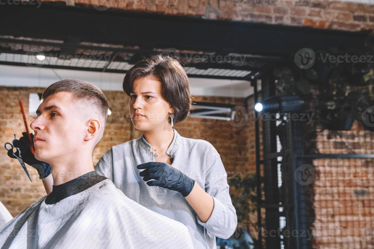 cabeleireira linda corta o cabelo da cabeça da cliente com um aparador elétrico na barbearia. publicidade e conceito de barbearia. lugar para texto ou publicidade foto