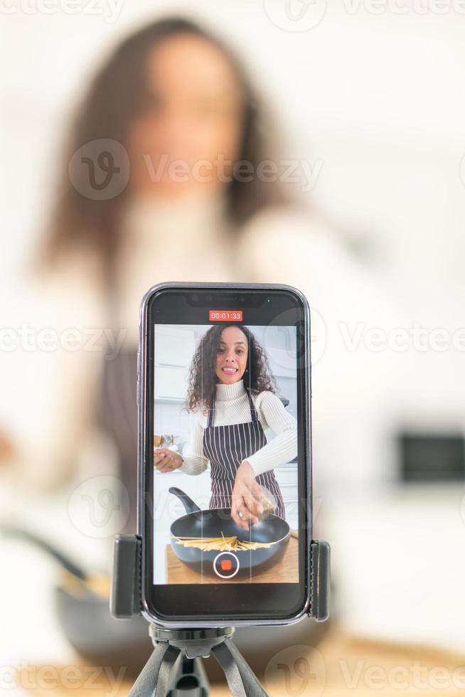 mulher latina gravando vídeo e cozinhando na cozinha foto
